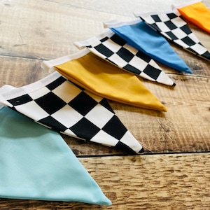 May include: A selection of fabric pennant flags in various colours and patterns. The flags include solid colours such as blue, yellow, and orange, and a black and white chequered design. Each flag has white trim and is arranged diagonally.