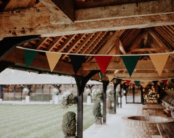 Op de afbeelding: Een rustiek houten gebouw met een reeks kleurrijke driehoekige vlaggen die aan het plafond hangen. De vlaggen zijn rood, geel, groen en blauw. Het gebouw heeft een houten dak en houten balken. Er is een grasveld buiten het gebouw.
