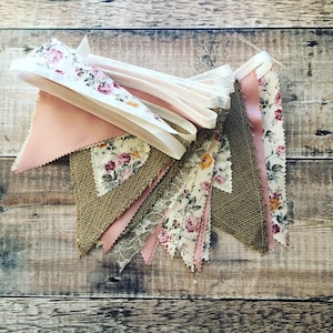 Könnte beinhalten: Eine Wimpelkette mit rosa, braunen und weißen Stoffdreiecken. Jedes Dreieck hat ein Blumenmuster. Die Wimpelkette ist mit weißem Band zusammengefügt.