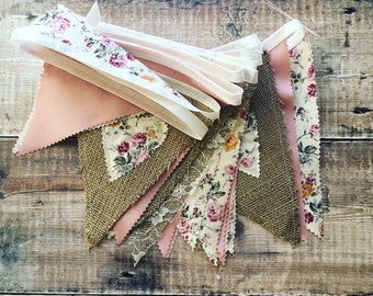 May include: A bunting banner with pink, brown, and white fabric triangles. Each triangle features a floral pattern. The bunting is strung together with white ribbon.