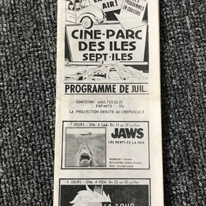 May include: Black and white poster advertising a drive-in movie theater called "Cine-Parc des Iles Sept-Iles". The poster features a car driving into the theater and lists the movies playing: "Jaws" and "The Towering Inferno".