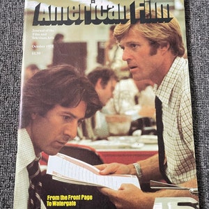 May include: A magazine cover featuring two men, one with a plaid shirt and the other with a blue tie. The magazine is titled "American Film" and the text "Journal of the Film and Television Arts" is printed below the title. The cover also includes the text "October 1975" and "$1.50". The text "From the Front Page to Watergate" is printed at the bottom of the cover.