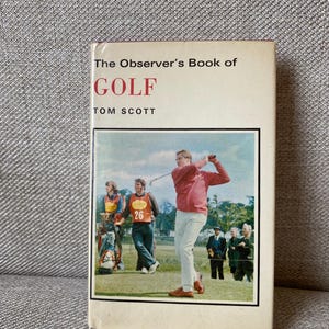 Puede incluir: Un libro antiguo titulado "The Observer's Book of GOLF" de Tom Scott. La portada presenta una fotografía de un golfista en acción, con espectadores y caddies en el fondo. El título está en rojo.