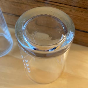 Op de afbeelding: Transparante glazen tumbler met een dikke bodem en een licht uitlopende rand. Het glas heeft een glad, transparant uiterlijk, met ge&euml;tste markeringen langs de zijkant. De bodem van het glas heeft de tekst "TEMPERED".