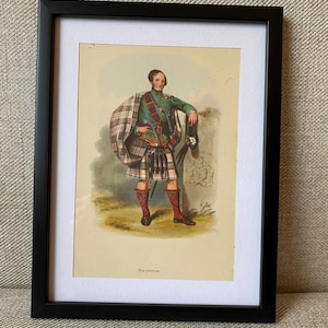 May include: A framed print depicting a man in traditional Scottish Highland dress, wearing a green jacket and a red sash. He is holding a sword and a hat. The print is titled "Macpherson".