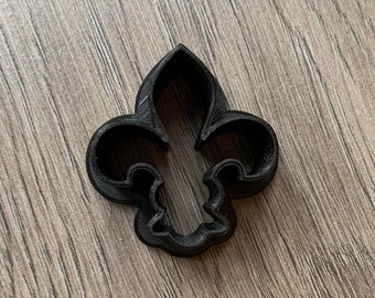 Könnte beinhalten: Schwarzer Plastik-Ausstecher in Form einer Fleur-de-lis.