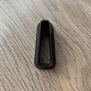 Op de afbeelding: Een zwart plastic voorwerp met een rechthoekige opening in het midden. Het voorwerp is gevormd als een hoge, smalle rechthoek.