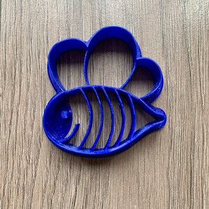 Op de afbeelding: Een blauwe plastic koekjesvormer in de vorm van een vis met een kroon op zijn kop.