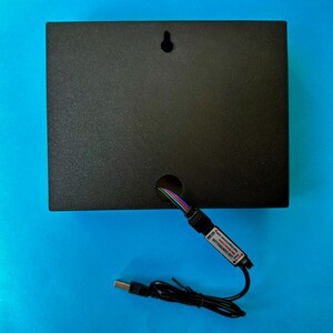 May include: A black rectangular box with a hole for wires and a keyhole for hanging. A USB cable and an LED controller are connected to the box. The background is a solid blue.