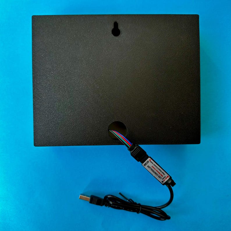 May include: A black rectangular box with a hole for wires and a keyhole for hanging. A USB cable and an LED controller are connected to the box. The background is a solid blue.