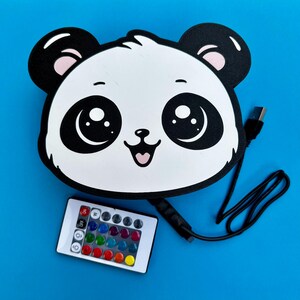 May include: A panda-shaped LED light with a black outline, white face, and black ears. The light has large, expressive eyes and a smiling mouth. A remote control with color options and a USB cable are included.
