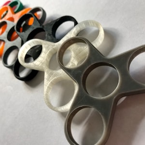 Puede incluir: Un conjunto de cinco spinners de dedos en diferentes colores, incluyendo rojo, verde, naranja, blanco y gris. Los spinners están hechos de plástico y tienen un diseño de tres puntas.