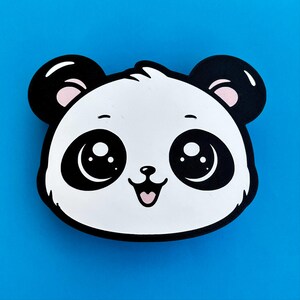 May include: A cartoon panda face with a black outline, black ears, and large black eyes with white highlights. The panda has a white face with pink accents on the ears and a smiling pink mouth. The background is a solid blue.