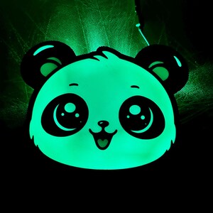 May include: A glowing panda face with large, expressive eyes and a smiling mouth. The panda's face is a bright, luminous green, with black accents on the ears and around the eyes. The background is dark.