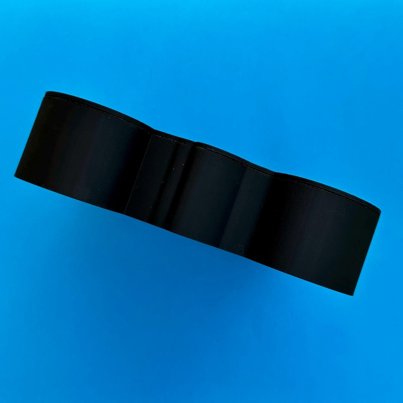 May include: A black wallet with a tri-fold design. The wallet is made of a smooth material and has a simple, minimalist style. The background is a solid blue.