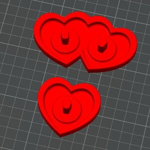 May include: Two red heart-shaped objects, one a single heart and the other two hearts joined together. Each heart has a circular design in the center. The objects are on a gray grid background.