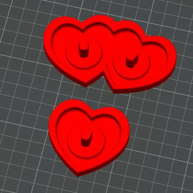 May include: Two red heart-shaped objects, one a single heart and the other two hearts joined together. Each heart has a circular design in the center. The objects are on a gray grid background.