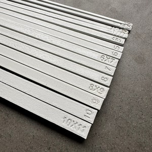 May include: A set of white wooden dowels with different sizes marked on them. The dowels are arranged in order of size, with the smallest dowel at the top and the largest dowel at the bottom. The sizes are marked in inches, with the smallest dowel being 4x5 inches and the largest dowel being 10x11 inches.