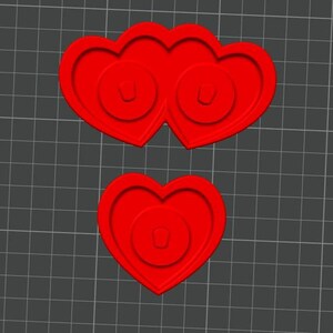 May include: Red heart-shaped craft supplies. One is a pair of conjoined hearts, and the other is a single heart. Each heart has a circular design in the center.