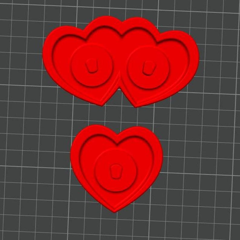 May include: Red heart-shaped craft supplies. One is a pair of conjoined hearts, and the other is a single heart. Each heart has a circular design in the center.