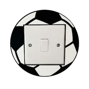 Könnte beinhalten: Ein weißer Lichtschalter mit einem schwarz-weißen Fußball-Design. Der Schalter hat zwei Tasten und einen Kippschalter.