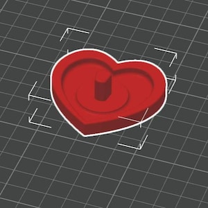 May include: A red heart-shaped object with a cylindrical protrusion in the center. The object has a white outline and is set against a gray grid background. The design appears to be a 3D model or a mold.