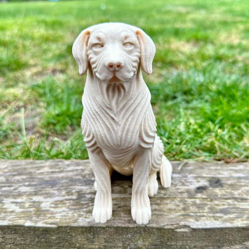 May include: A cream-colored dog figurine in a seated position. The dog has detailed fur texture and a gentle expression. The figurine is placed on a wooden surface with a green grassy background.