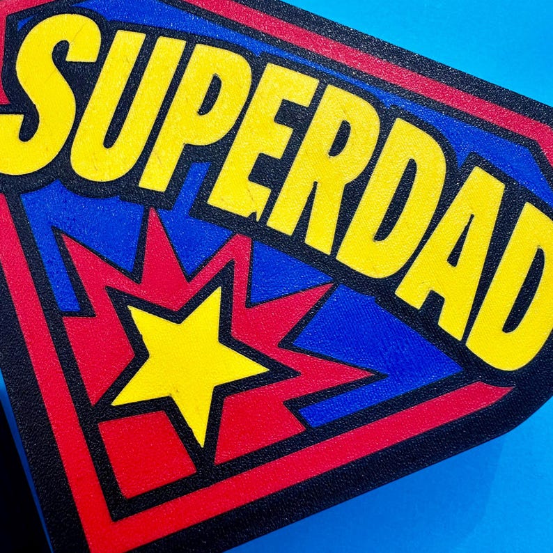 May include: A rectangular patch with the words "SUPERDAD" in large yellow letters. The patch has a blue background with a red and yellow starburst design and a yellow star in the center. The border is red and black.
