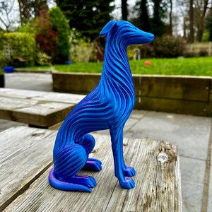 May include: A blue and purple decorative dog sculpture with a textured, wave-like design. The dog is sitting on a wooden surface. The sculpture has a sleek, modern aesthetic and is a decorative item.