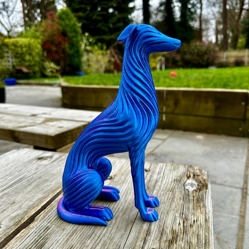 May include: A blue and purple decorative dog sculpture with a textured, wave-like design. The dog is sitting on a wooden surface. The sculpture has a sleek, modern aesthetic and is a decorative item.