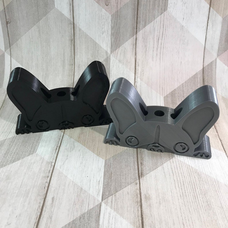 May include: Two 3D printed dog head pencil holders. One is black and the other is gray. Both have a hole in the top for pencils.