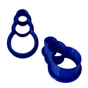May include: Two blue plastic snowman-shaped cookie cutters. The cutters are made of solid blue plastic and have a three-dimensional design. The snowman shape is made up of three stacked circles.