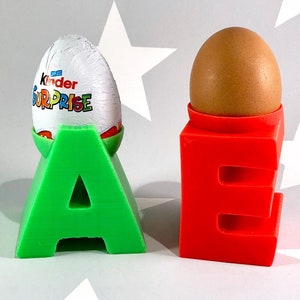 Può includere: Due porta uova stampati in 3D a forma delle lettere A ed E. La A è verde e contiene un uovo di cioccolato Kinder Surprise. La E è rossa e contiene un uovo marrone.