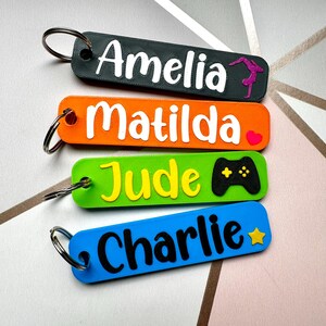 Puede incluir: Cuatro llaveros coloridos con nombres: Amelia, Matilda, Jude y Charlie. Cada llavero tiene un color y dise&ntilde;o diferente. El de Amelia es gris oscuro con una gimnasta, el de Matilda es naranja con un coraz&oacute;n, el de Jude es verde con un mando de videojuegos y el de Charlie es azul con una estrella.