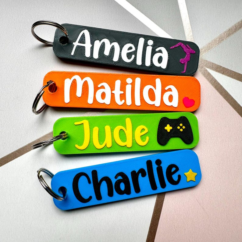 Puede incluir: Cuatro llaveros coloridos con nombres: Amelia, Matilda, Jude y Charlie. Cada llavero tiene un color y dise&ntilde;o diferente. El de Amelia es gris oscuro con una gimnasta, el de Matilda es naranja con un coraz&oacute;n, el de Jude es verde con un mando de videojuegos y el de Charlie es azul con una estrella.
