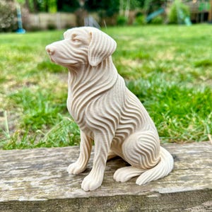May include: A cream-colored, carved dog figurine in a sitting position. The dog has a detailed, textured design with wavy lines across its body. The figurine is placed on a wooden surface with a grassy background.