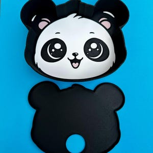 May include: A black and white panda-shaped tray and a matching panda-shaped base, both with a cute cartoon face. The tray has a white face with black eyes, ears, and a pink mouth. The base is solid black with a blue circle.