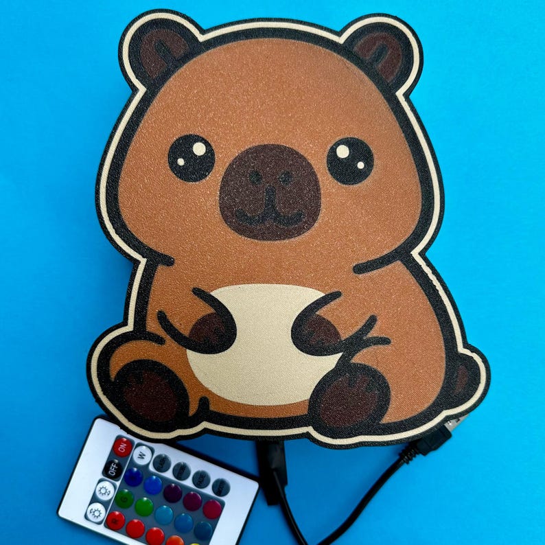 May include: A brown bear-shaped LED night light with a white border, black eyes, and a dark brown nose. A remote control with multiple color options is included. The night light is connected to a USB cable.