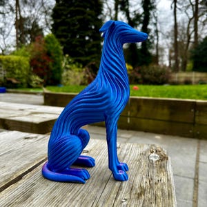 May include: A blue decorative dog sculpture with a unique, wave-like design. The dog is sitting on a wooden surface. The sculpture is a vibrant shade of blue, with a smooth, glossy finish. The dog's form is sleek and elegant.