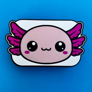 K&ouml;nnte beinhalten: Ein rosa Axolotl-Cartoon-Design mit gro&szlig;en schwarzen Augen, rosa Kiemen und einem kleinen L&auml;cheln. Das Axolotl ist vor einem wei&szlig;en Hintergrund mit schwarzer Umrandung auf blauem Grund platziert.