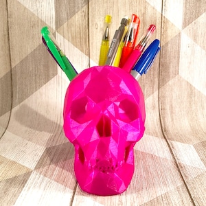 May include: A pink geometric skull-shaped desk organiser with colourful pens sticking out of the top.