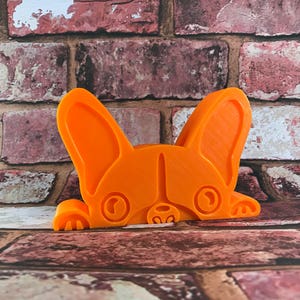 May include: Orange plastic doorstop shaped like a French bulldog peeking out from behind a brick wall.