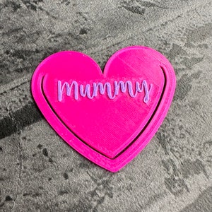 May include: A pink heart-shaped bookmark with the word "Mummy" written in purple lettering.