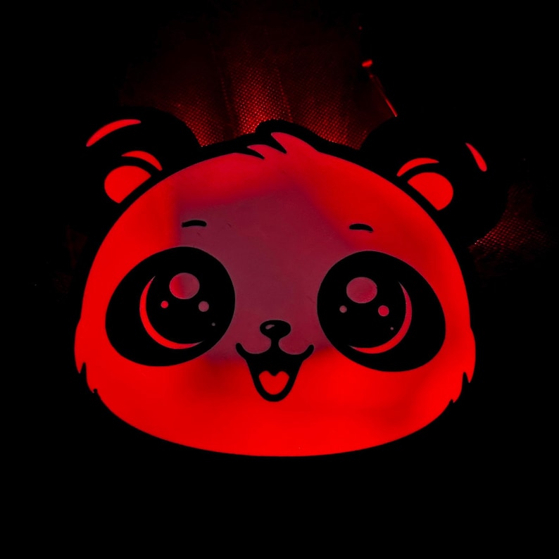May include: A red panda face with large, black eyes and a smiling mouth. The panda's ears and facial features are outlined in black against a red background. The image is set against a black backdrop.