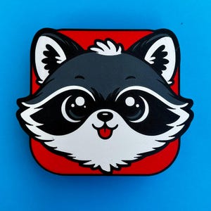 May include: A cartoon raccoon face with large eyes, a black mask, and a red tongue, set against a red square. The raccoon is primarily black and white, with a small tuft of white hair. The background is a solid blue.