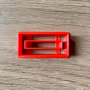 Può includere: Tagliapasta in plastica rossa a forma di rettangolo con un rettangolo più piccolo tagliato all'interno.