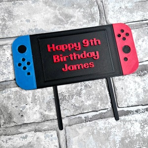 May include: A black and red Nintendo Switch cake topper with the text "Happy 9th Birthday James" in red.