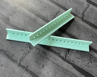 May include: Two light green plastic rulers with holes along the edges. The rulers are angled and overlapping.