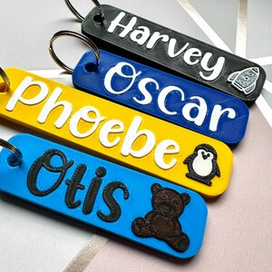 Puede incluir: Cuatro llaveros personalizados en negro, azul, amarillo y azul. Cada llavero tiene un nombre en un color contrastante: "Harvey", "Oscar", "Phoebe" y "Otis". Iconos decorativos: cohete, ping&uuml;ino y oso de peluche.
