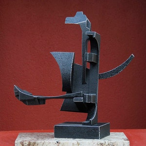 May include: Abstract metal sculpture with a black finish. The sculpture is composed of geometric shapes and is mounted on a granite base.